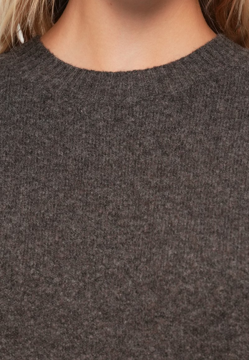 Pull en laine gris foncé avec un col rond côtelé et une finition douce et texturée. Le tissu semble chaud et confortable.