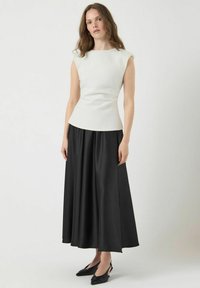 Bílý bezramínkový top s přiléhavým korzetem a černou saténovou maxi sukni, která má splývavý design a minimalistický, elegantní siluetu.