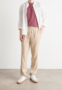 Lätta beige linnbyxor med elastisk midja; kombinerat med en murrig texturerad skjorta och en vit skjorta med knappar. Sneakers är vita med beige detaljer.