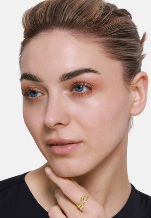 Goldring mit geometrischem Design am Finger des Modells, das dreieckige und Zickzackmuster aufweist. Das Modell hat helle Haut und kurze Haare.
