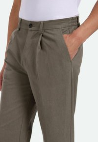Pantalones caqui de corte relajado, con pliegues delanteros, cierre de un botón y bolsillos laterales. Fabricados en una tela suave y ligera.
