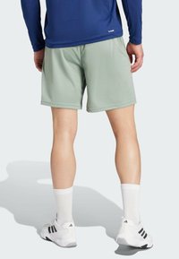 Hellgrüne Sportshorts mit glatter Textur, ausgestattet mit einem elastischen Bund und seitlichen Taschen. Getragen mit weißen Socken und Schuhen mit schwarzen Akzenten.