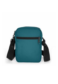 Modrý přehozený batoh z hladké látky, s horním zipem, přední kapsou a nastavitelným černým popruhem.