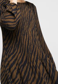 Brun och svart mönstrad klänning med långa puffärmar, som har vertikala ränder och en slät, draperad textur. Elegant, flödande design.