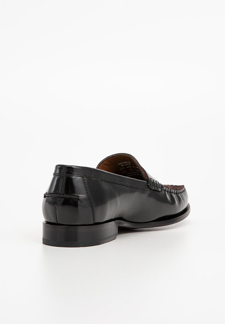 Des mocassins en cuir noir présentent un bout rond, des coutures décoratives et une finition lisse, avec un talon plat et un design classique.