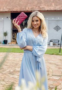 Světle modré šaty s dlouhým rukávem, na manžetách nařasené, s páskem v pase, doplněné o texturovanou kabelku v tmavě růžové barvě s diamantovým vzorem.
