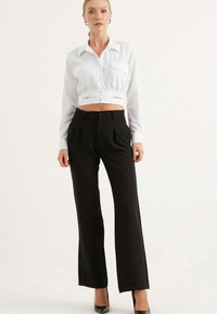 Vit kortärmad skjorta med två framfickor, kombinerad med högmidjade svarta vida byxor. Svarta klackar fulländar looken.