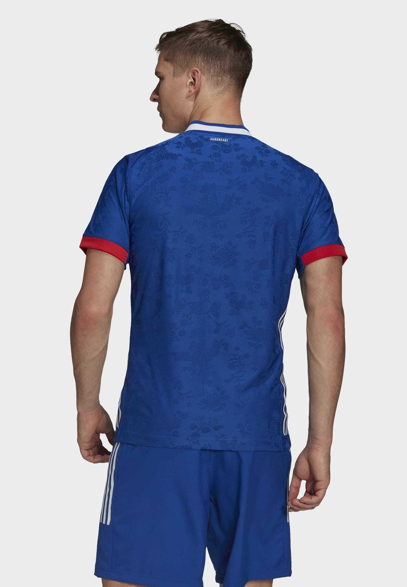 Blauwe voetbaltop met een bloemenpatroon, rode mouwboorden, witte kraag, en het "AEROREADY" logo op de achterkant. Gecombineerd met blauwe shorts.