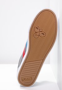 Gray sneaker sole with herringbone pattern, featuring blue, red, and white accents, and a logo imprint. Textured rubber for grip.