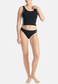 Svart kort tanktop och matchande bikiniunderdel med vita sidostreck och logotypdetaljer. Slät tyg, åtsittande design, minimalistisk stil.