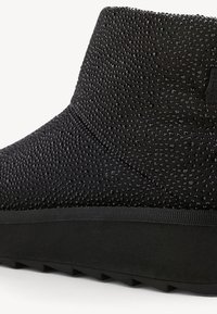 Bottine noire recouverte de petits strass noirs avec une semelle épaisse texturée et une bordure en tissu au-dessus de la semelle.