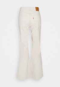 Jeans blancs évasés en denim, avec une étiquette de marque en cuir, deux poches arrières et une finition texturée.