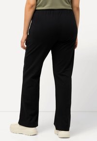 Zwarte, aansluitende broek van zacht materiaal met een elastische tailleband, eenvoudige desig en een rechte pijp. Gemaakt met beige sneakers.