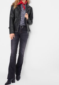 Svart läderjacka med dragkedjefickor, mönstrad blå skjorta, mörka utsvängda jeans och svarta ankelstövlar. Röd bandana knuten runt halsen.