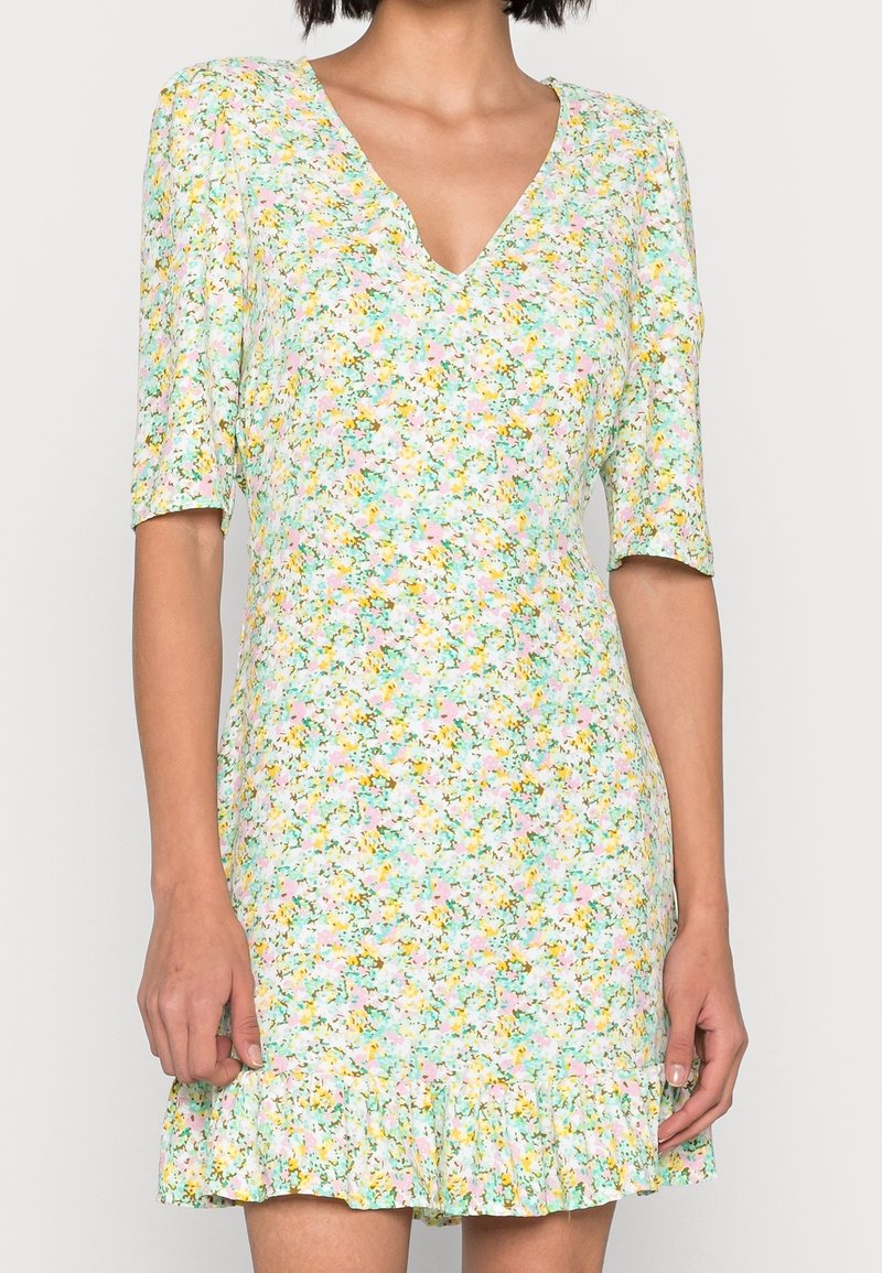 Robe fleurie avec un col en V, des manches courtes, confectionnée en tissu léger. Elle présente un ourlet à volants et un mélange de couleurs pastel incluant le vert, le rose et le jaune.