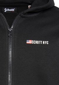 Felpa nera con zip realizzata in un materiale morbido. Presenta una zip frontale, cappuccio e un logo con una bandiera degli Stati Uniti e "SCHOTT NYC" in lettere bianche.
