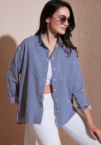 Camicia a righe blu e bianca, con taschino sul petto a righe diagonali, maniche arrotolate e un taglio rilassato.
