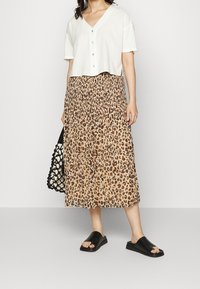 Top blanco recortado con botones, falda midi plisada de estampado animal en beige y marrón, sandalias de tiras negras y un bolso de mano trenzado negro.