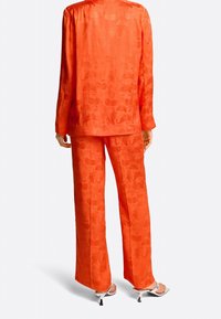 Un ensemble deux pièces orange en tissu texturé avec de subtils motifs floraux. Le haut a des manches longues et une coupe ample, associé à un pantalon à jambes larges.