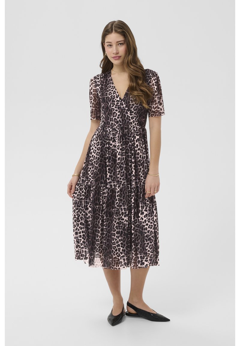 Woman wearing a knee-length, short-sleeve leopard print dress with black slingback flats, standing against a plain light background.