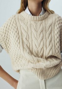 Stickad kabeltröja i mjuk beige, med korta ärmar, ribbad kant och invecklade texturerade mönster på kroppen. Lätt och löst sittande.