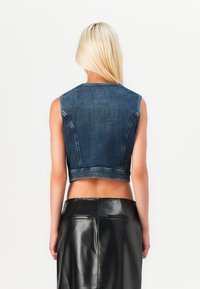 Denim prerezan telovnik s brezrokavnim dizajnom, surovimi robovi in temnim pranjem. V kombinaciji s krojenim črnim usnjenim krilom, ki poudarja eleganten silhuet.