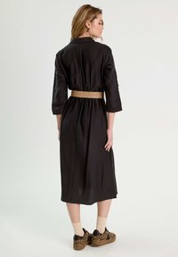 Robe noire à mi-longueur avec des manches trois-quarts, cintrée à la taille par une ceinture tissée beige. Portée avec des baskets imprimé léopard.