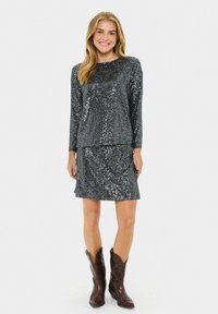 Conjunto de top y falda de lentejuelas en gris oscuro, con un corte relajado, mangas largas y una textura suave. Combinado con botas de vaquero marrones.