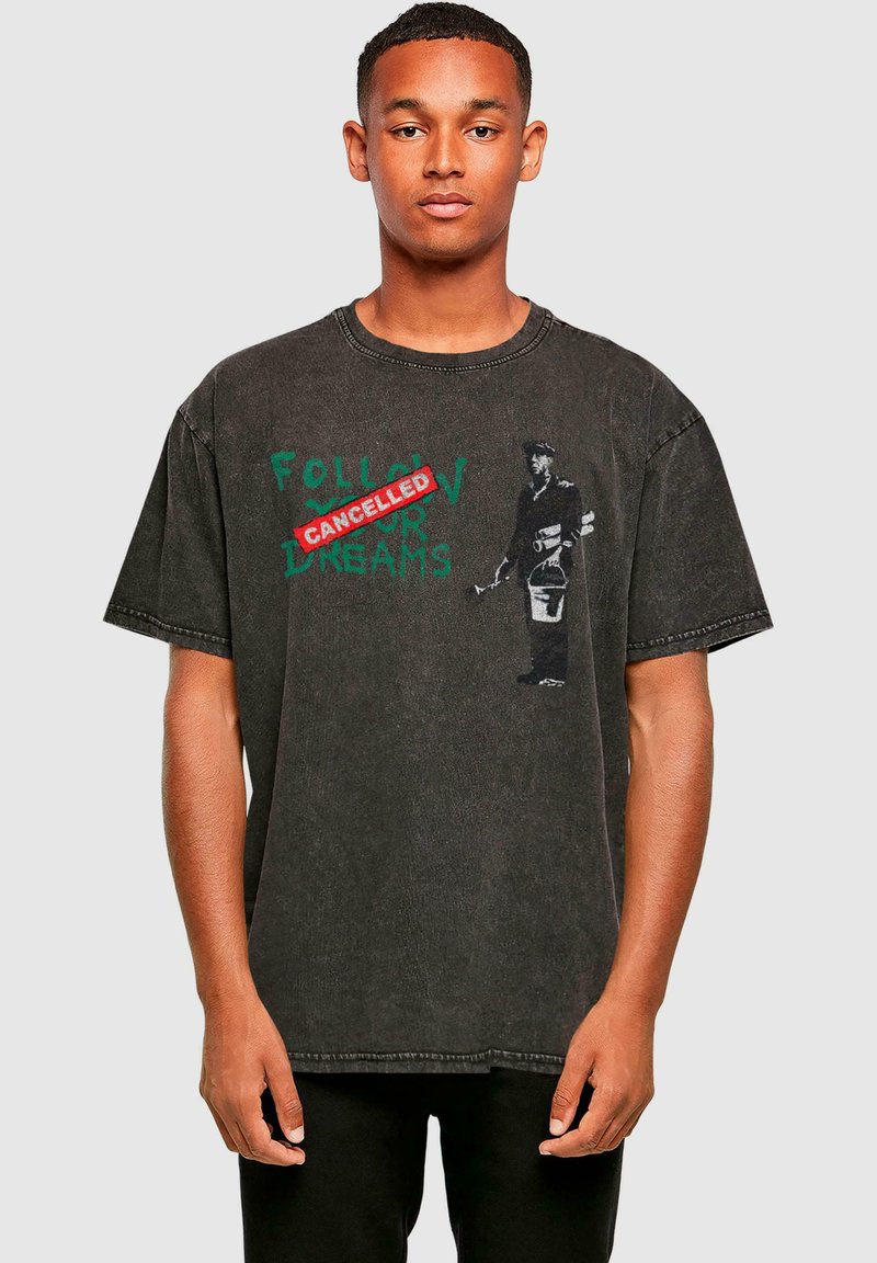 Schwarzes Baumwoll-T-Shirt mit lockerer Passform. Mit grünem Text "FOLLOW YOUR DREAMS" und einem roten "CANCELLED"-Stempel sowie einemgrafischen Druck.