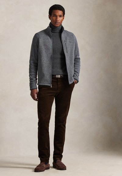 Γκρι μπουφάν με φερμουάρ και ψηλό γιακά, υφασμένο πουλόβερ με ζιβάγκο, καφέ παντελόνι κορντόρι και καφέ σουέντ μοκασίνια.