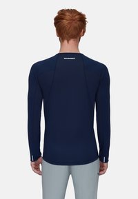 Marineblauwe sportshirt met lange mouwen, vlakke naden, raglanmouwen en logo op de achterkant. Beschikt over duimgaten bij de manchetten en een gladde, ademende stof.