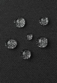 Wassertropfen auf einer strukturierten schwarzen Stoffoberfläche, unterschiedlich in Größe und Form, mit klarer, reflektierender Qualität und glattem Erscheinungsbild.