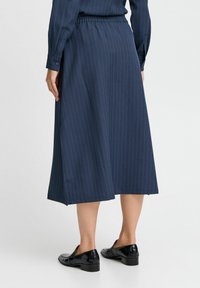 Jupe midi bleu marine avec motif à rayures, taille élastique et fentes latérales. Associée à des mocassins en cuir verni noir.