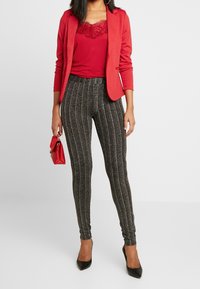 Röd topp med spetskant under en åtsittande röd blazer, matchad med svarta och silverrandiga leggings och svarta spetsiga klackskor. Röd handväska.