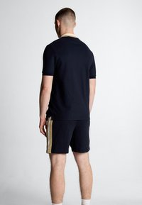 Polo shirt navy a maniche corte con colletto a contrasto; abbinato a pantaloni corti navy con strisce laterali dorate. Tessuto liscio, vestibilità casual.