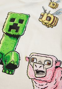 Weißes T-Shirt mit farbenfrohen Grafiken: eine grüne Blockfigur, ein pinkes Schaf und gelbe Bienen mit detaillierten Gesichtsausdrücken und Merkmalen.