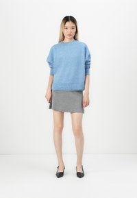 Maglione azzurro chiaro lavorato a maglia con scollo rotondo e orlo a costine, abbinato a una mini gonna grigia. Il modello indossa decolleté neri a punta.