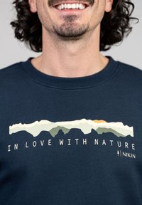 Navy sweatshirt met een bergafbeelding en de tekst "IN LOVE WITH NATURE" in het wit, met aardse tonen en een gestructureerde stof.