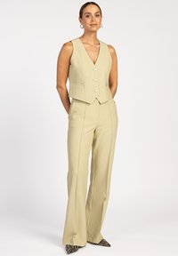 Ivory vest met een V-hals en knopen aan de voorkant, gecombineerd met hoge, uitlopende broeken. Draagt het met puntige, zwart-wit gestreepte schoenen.