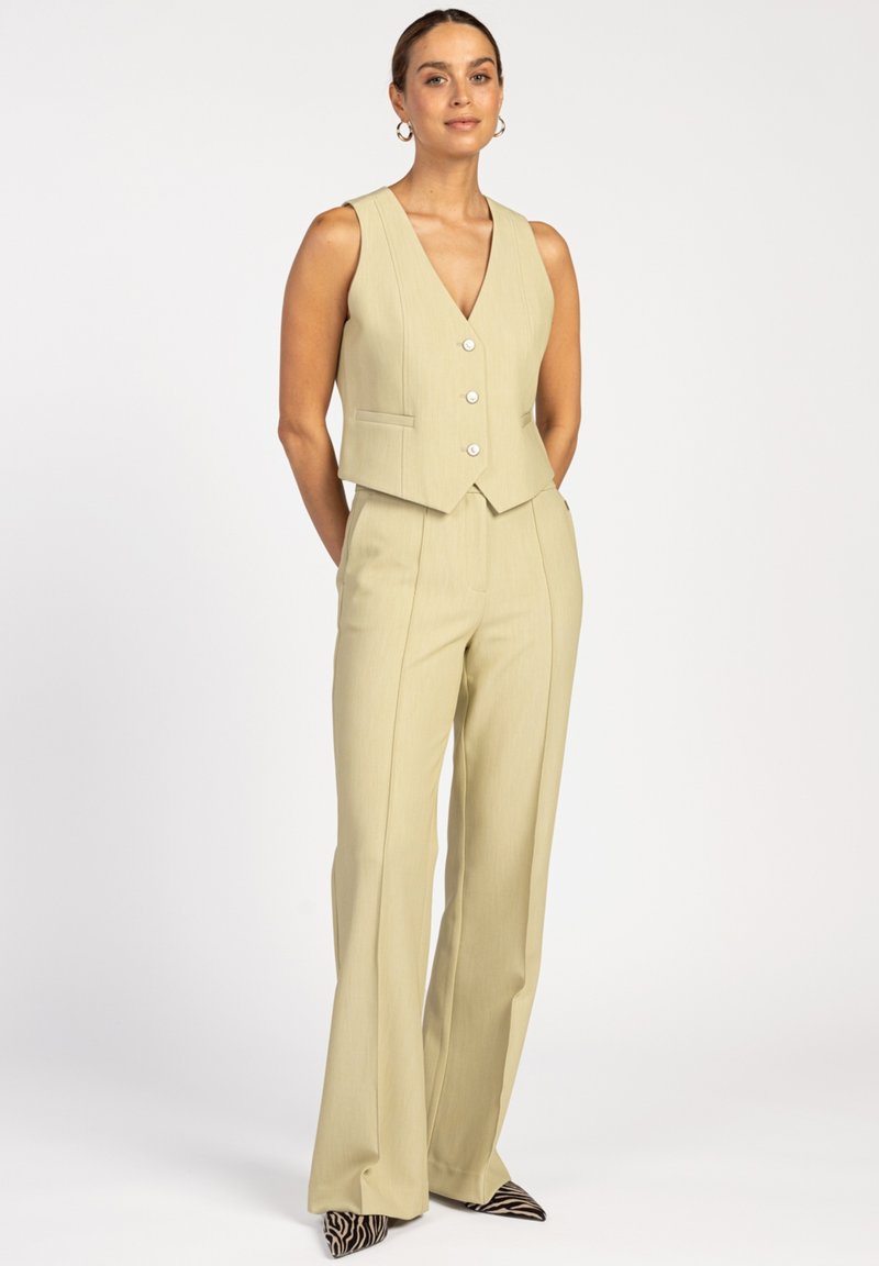 Ivory vest met een V-hals en knopen aan de voorkant, gecombineerd met hoge, uitlopende broeken. Draagt het met puntige, zwart-wit gestreepte schoenen.