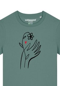 Grüne T-Shirt mit einer schwarzen Linzeichnung von Händen, die eine Blume und ein rotes Herz halten, betont ein minimalistisches Design und eine weiche Textur.