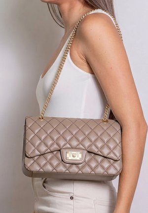 Femme portant un haut blanc sans manches porte un sac à bandoulière en cuir matelassé beige avec une chaîne dorée et un fermoir rectangulaire.