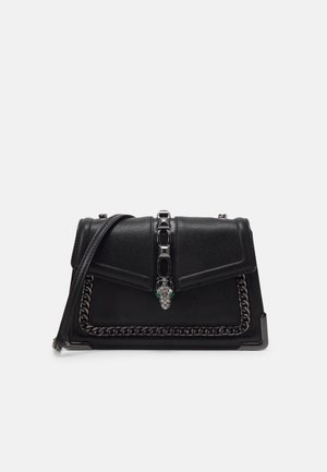 Sac à main en cuir noir avec garniture chaîne, une bandoulière et un fermoir tête de serpent orné de bijoux au centre devant.