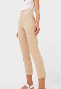 Beige high-waisted trousers with front pockets, tailored fit, and cropped length. Features clean lines and subtle side slits at the hem.