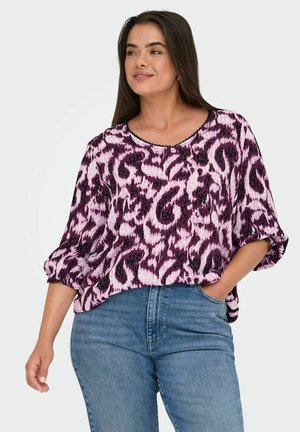 Ljubičasta i ružičasta blouse s uzorkom, labavog kroja, okruglim izrezom i elastičnim rukavima, u kombinaciji s plavim jeans hlačama visokog struka.