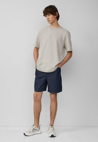 T-shirt gris clair à manches courtes, coupe décontractée, associé à un short bleu marine, de couleur unie, et des chaussures de sport blanches avec des accents gris.