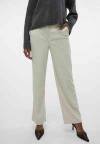 Lichtbeige wijde broek met ribbelstructuur, voorzien van zijzakken, gecombineerd met een donkergrijze gebreide trui en bruine puntige hakken.