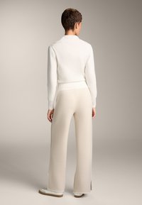 Pulover alb tricotat cu tiv ondulat, asortat cu pantaloni largi bej, cu fante pe laterale. Modelul poartă adidași albi.