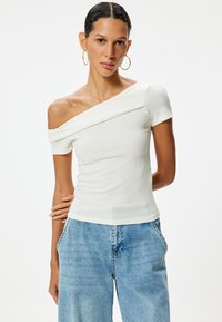 Witte off-shoulder ribgebreide top met korte mouwen, voorzien van een gedrapeerde halslijn en een aansluitende pasvorm, gecombineerd met lichtblauwe wijde jeans.