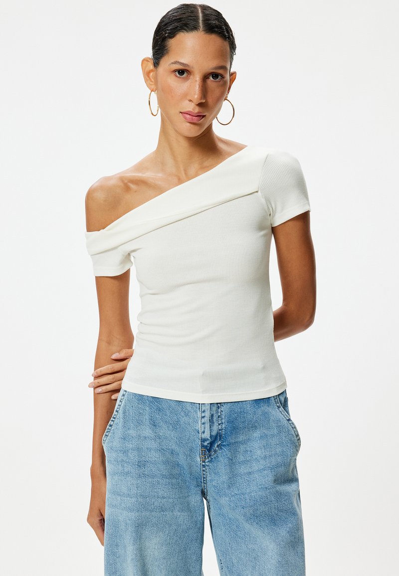 Witte off-shoulder ribgebreide top met korte mouwen, voorzien van een gedrapeerde halslijn en een aansluitende pasvorm, gecombineerd met lichtblauwe wijde jeans.